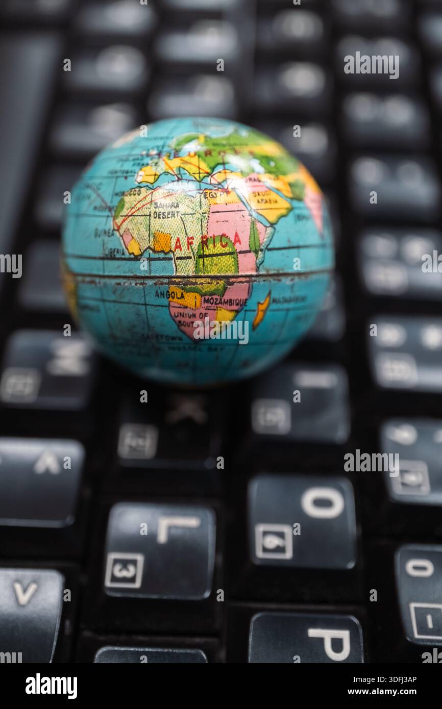 Ein kleiner Globus, der Afrika auf einer schwarzen Tastatur darstellt, symbolisiert globale Konnektivität und Technologie Stockfoto
