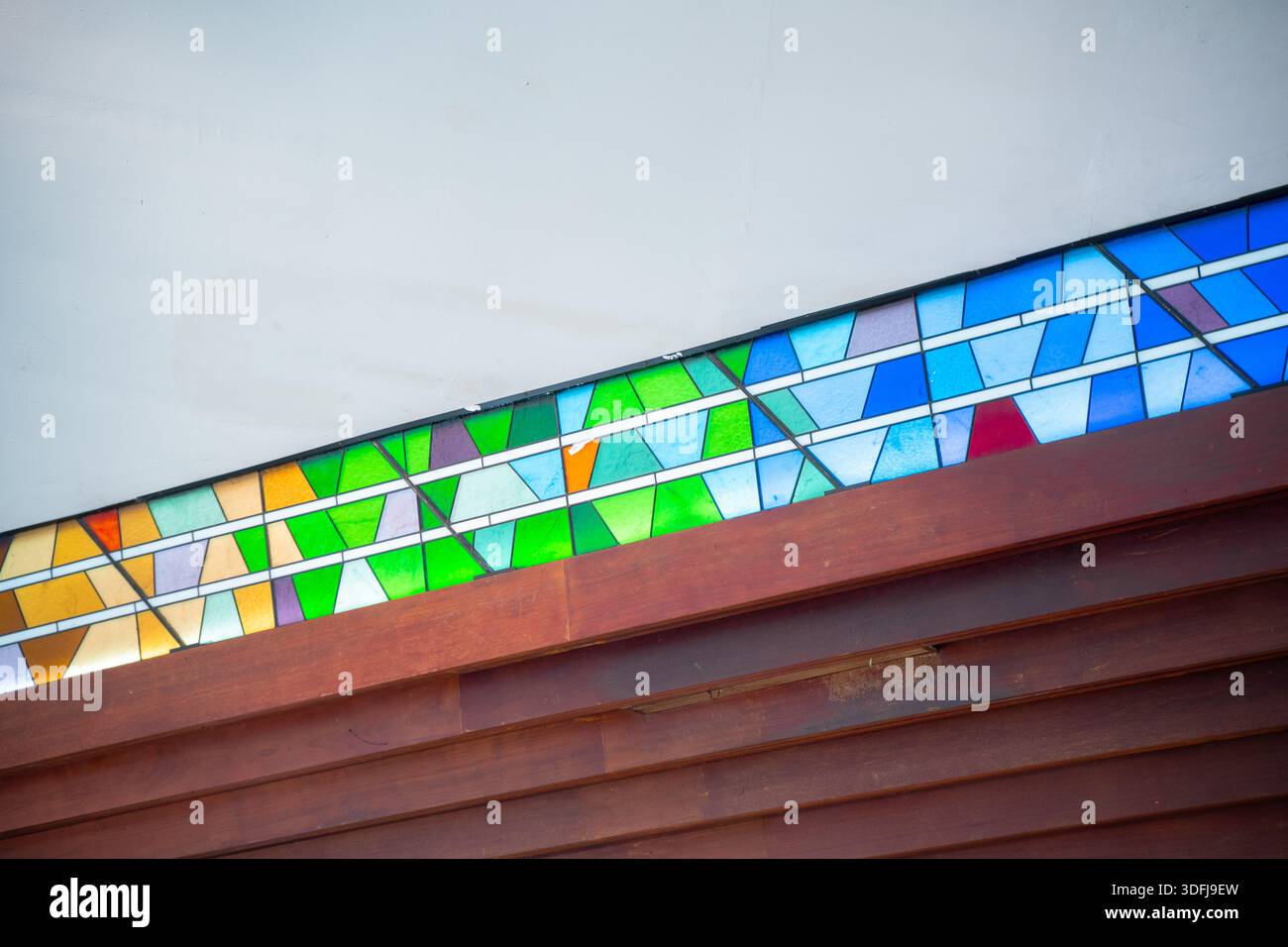 Langer Rand aus geometrischen Buntglasfenstern in Grün-, Blau- und Gelbtönen über einer dunklen Holztafel Stockfoto