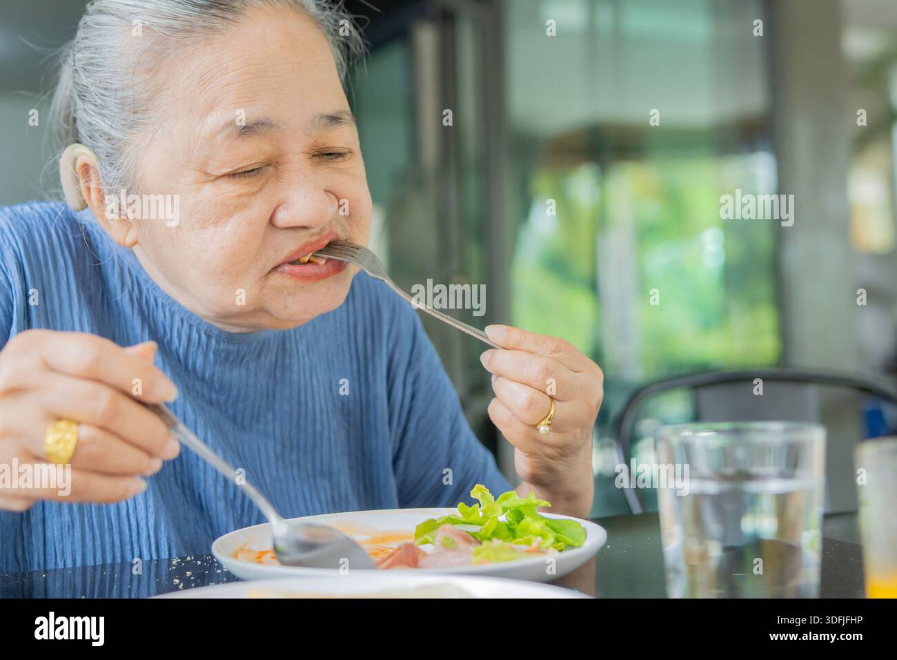 Asiatische Seniorin sitzt und genießt ihr gesundes Frühstück zu Hause. Gesundes Lebensmittelkonzept. Selektiver Fokus. Stockfoto