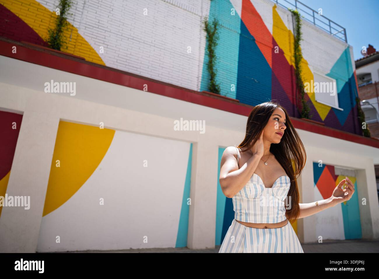 Junge Frau posiert am sonnigen Tag, umgeben von lebendiger Straßenkunst und geometrischen Formen Stockfoto