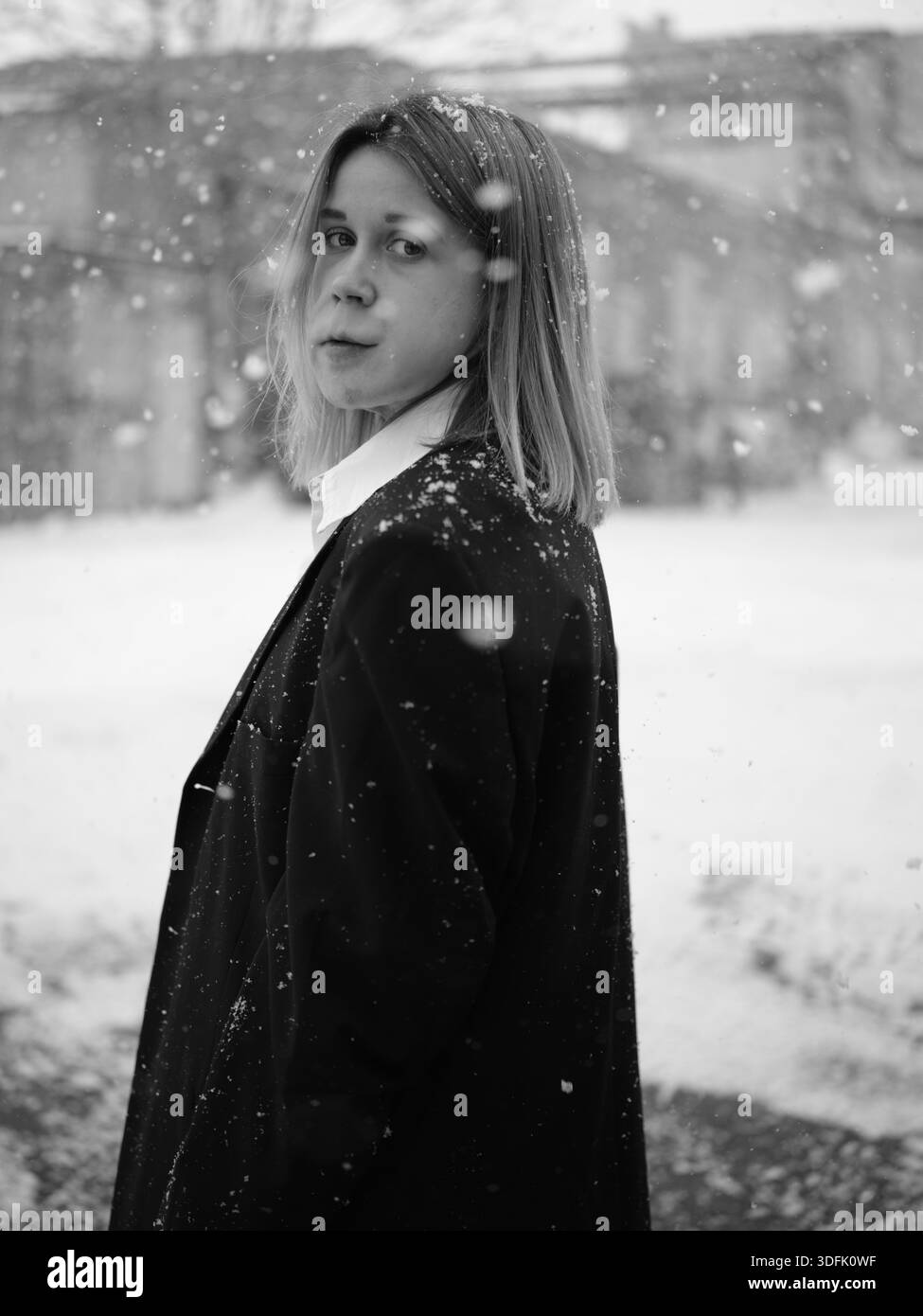 Einfarbiges Porträt einer Frau mit Portweinfleck, die während des Schneefalls in die Kamera schaut. Empowerment- und Diversitätskonzept im urbanen Winterumfeld Stockfoto