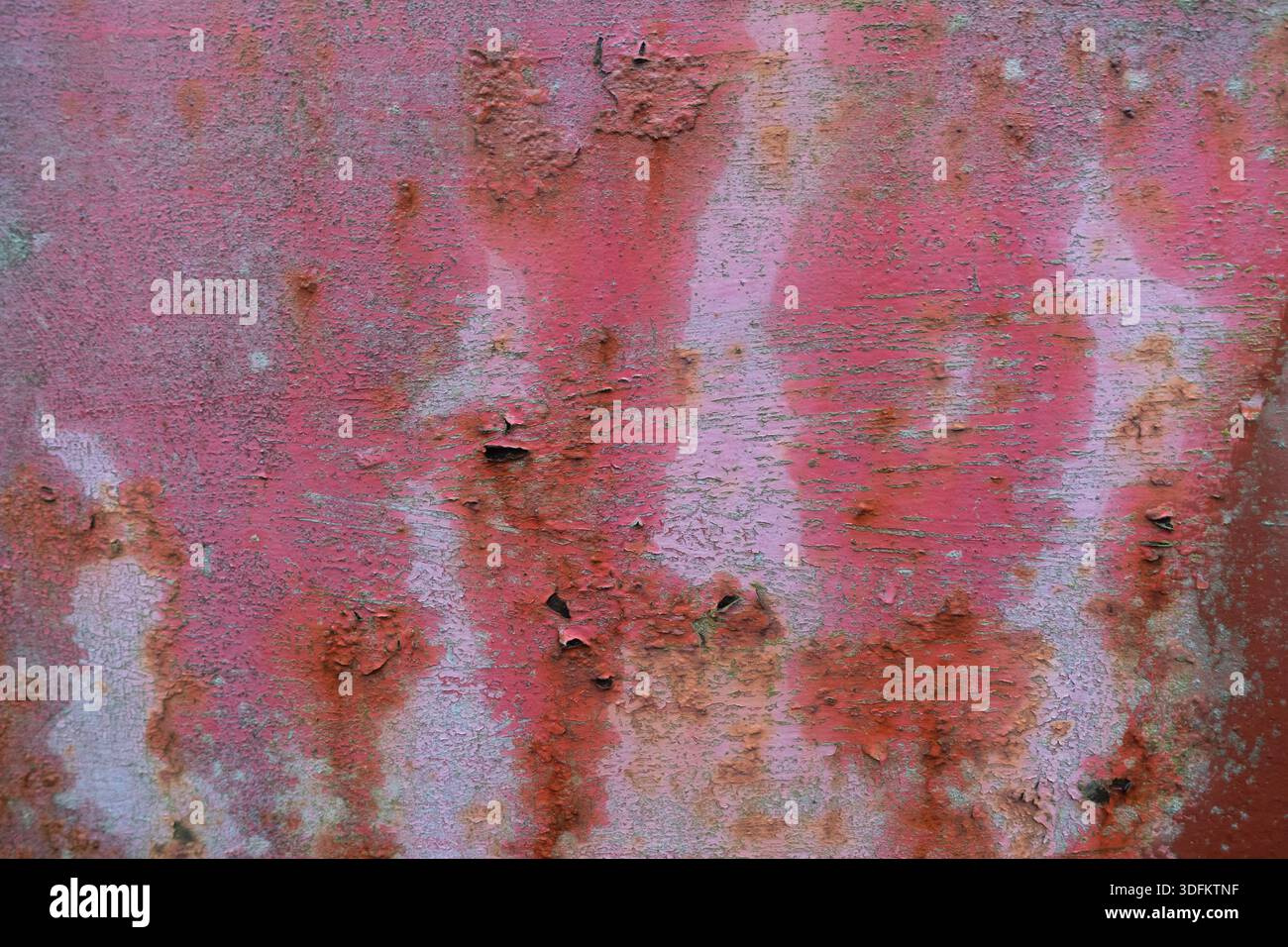 Verwitterte pinkfarbene Wand mit abblätternder Farbe, Rostflecken und rauer Textur, die urbanen Verfall und veraltete architektonische Oberfläche zum Ausdruck bringt Stockfoto