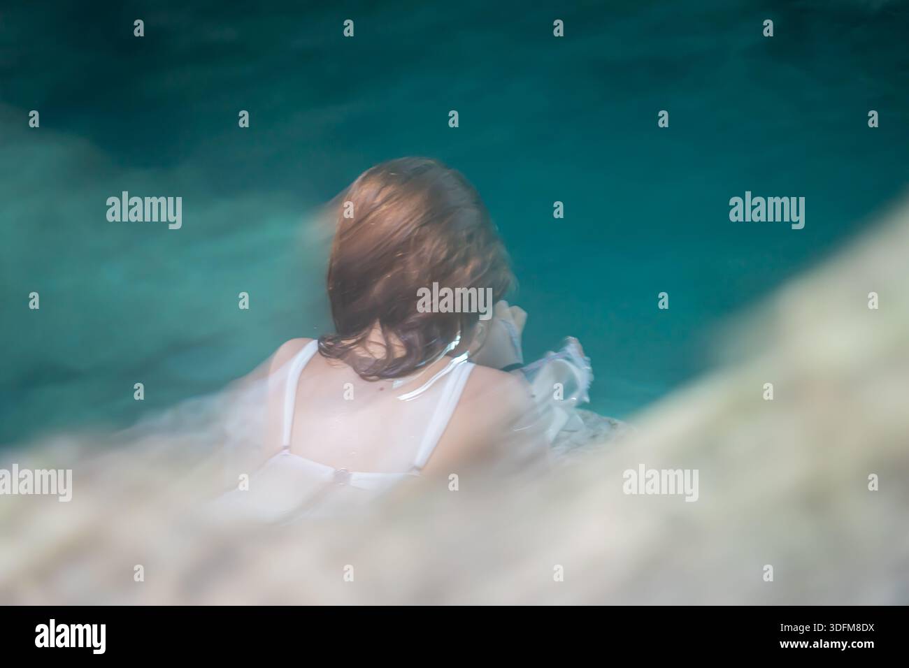 Person im Wasser, mit einer traumhaften, ätherischen Ästhetik. Der Hintergrund ist in leuchtendem Petrol gehalten Stockfoto