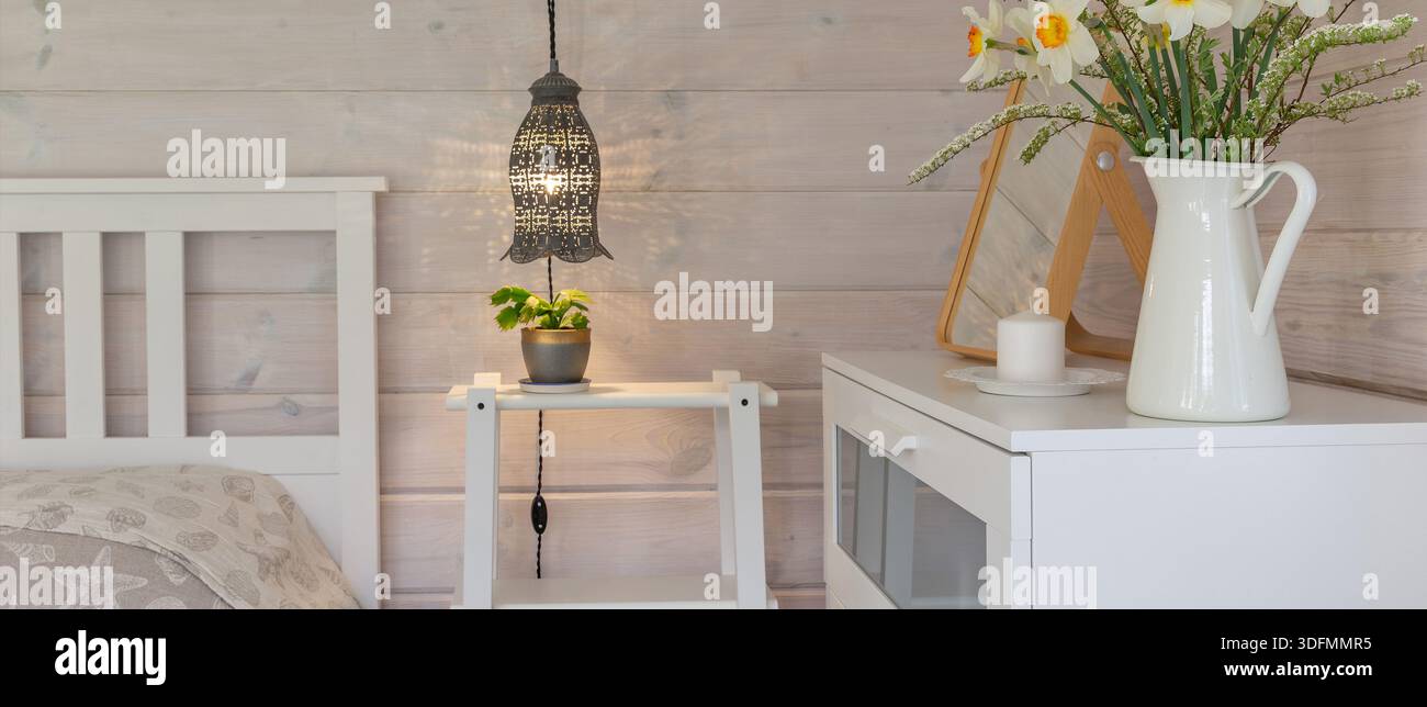 Gemütliches skandinavisches Panoramafenster mit warmer Pendelleuchte, Kerze und Frühlingsblumen Stockfoto