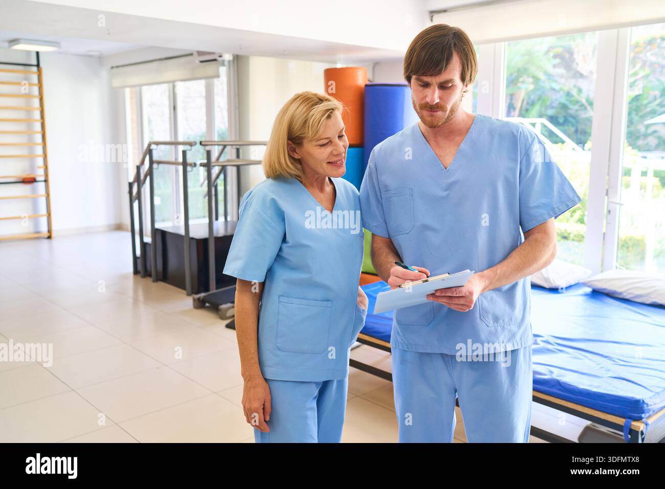Ein Physiotherapeut und eine ältere Frau prüfen in einem Reha-Zentrum Notizen, in denen der Behandlungsplan und der Fortschritt der Heilung in Innenräumen diskutiert werden. Dieses Bild kann Stockfoto