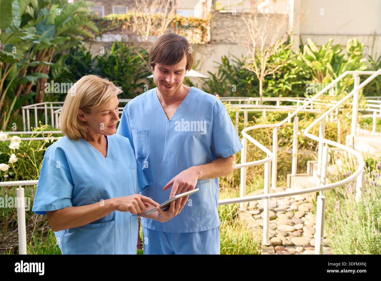 Zwei Physiotherapeuten prüfen Patientendaten auf einem Tablet im Freien in einem Rehabilitationszentrum. Sie besprechen den Behandlungsplan für einen älteren Vater Stockfoto