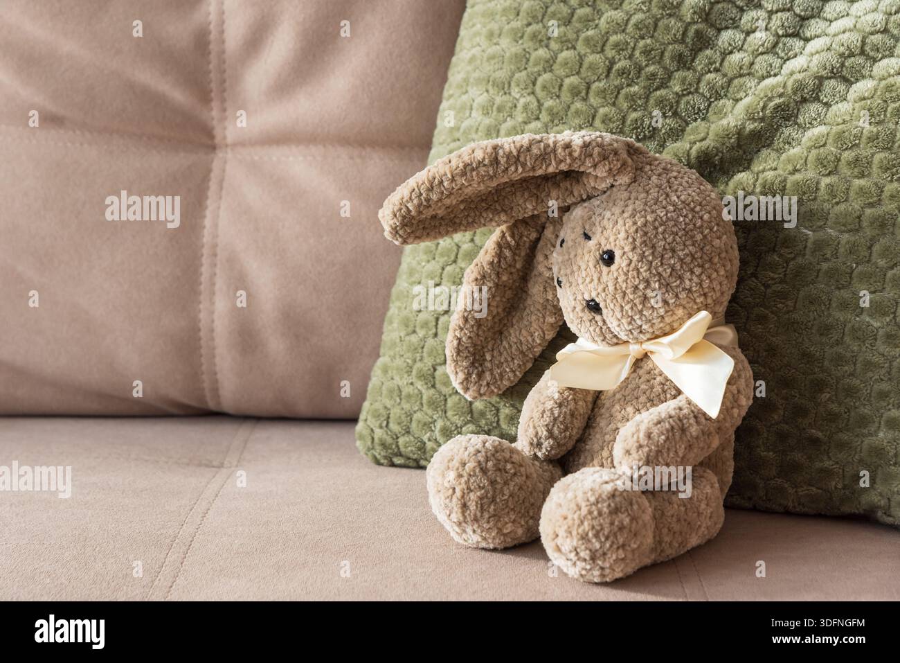 Plüschhase auf Sofa mit grünem Kissen. Gemütlicher, Von Kindheit Inspirierter Hintergrund Stockfoto