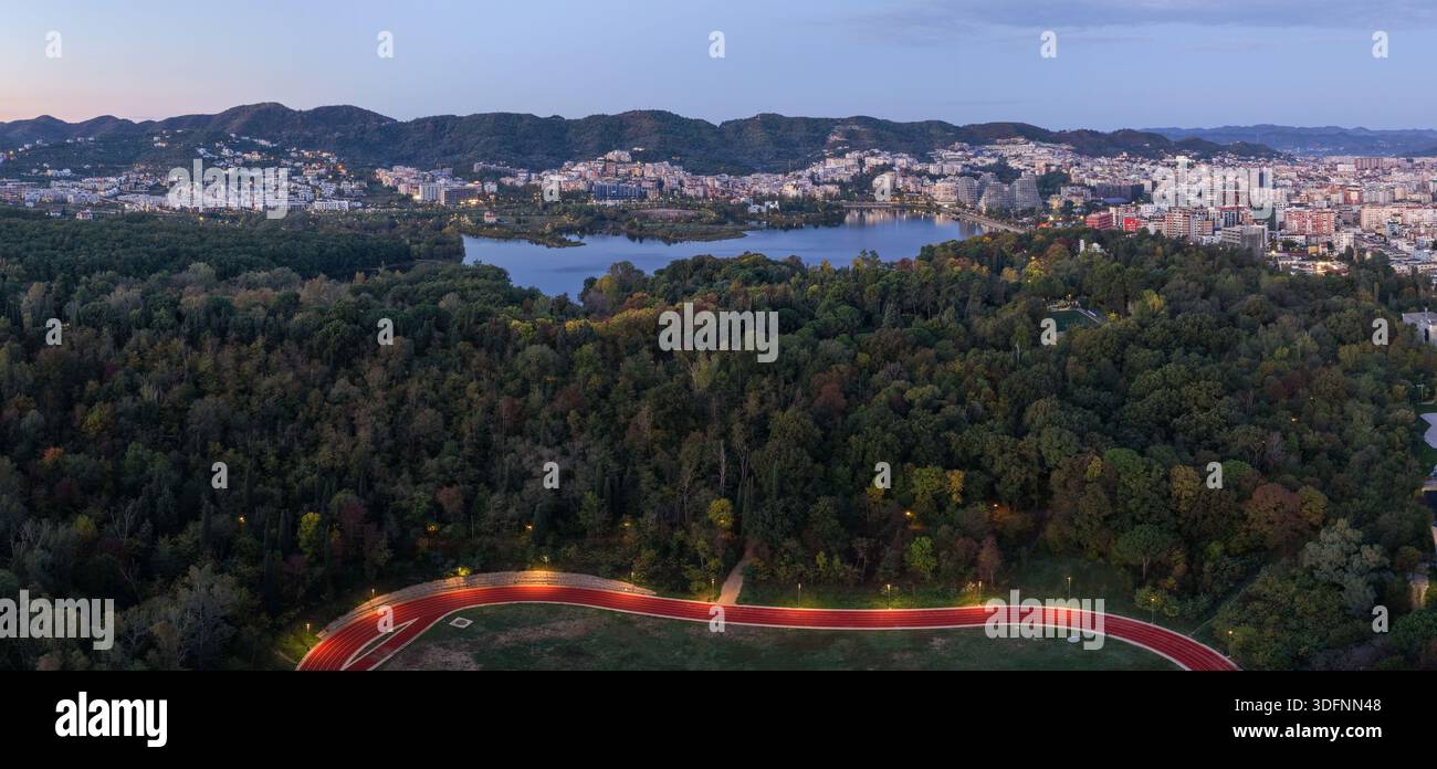 Ein Blick auf den künstlichen See von Tirana, der von dichtem herbstfarbenem Wald umgeben ist, und die Skyline der Stadt dahinter. Stockfoto