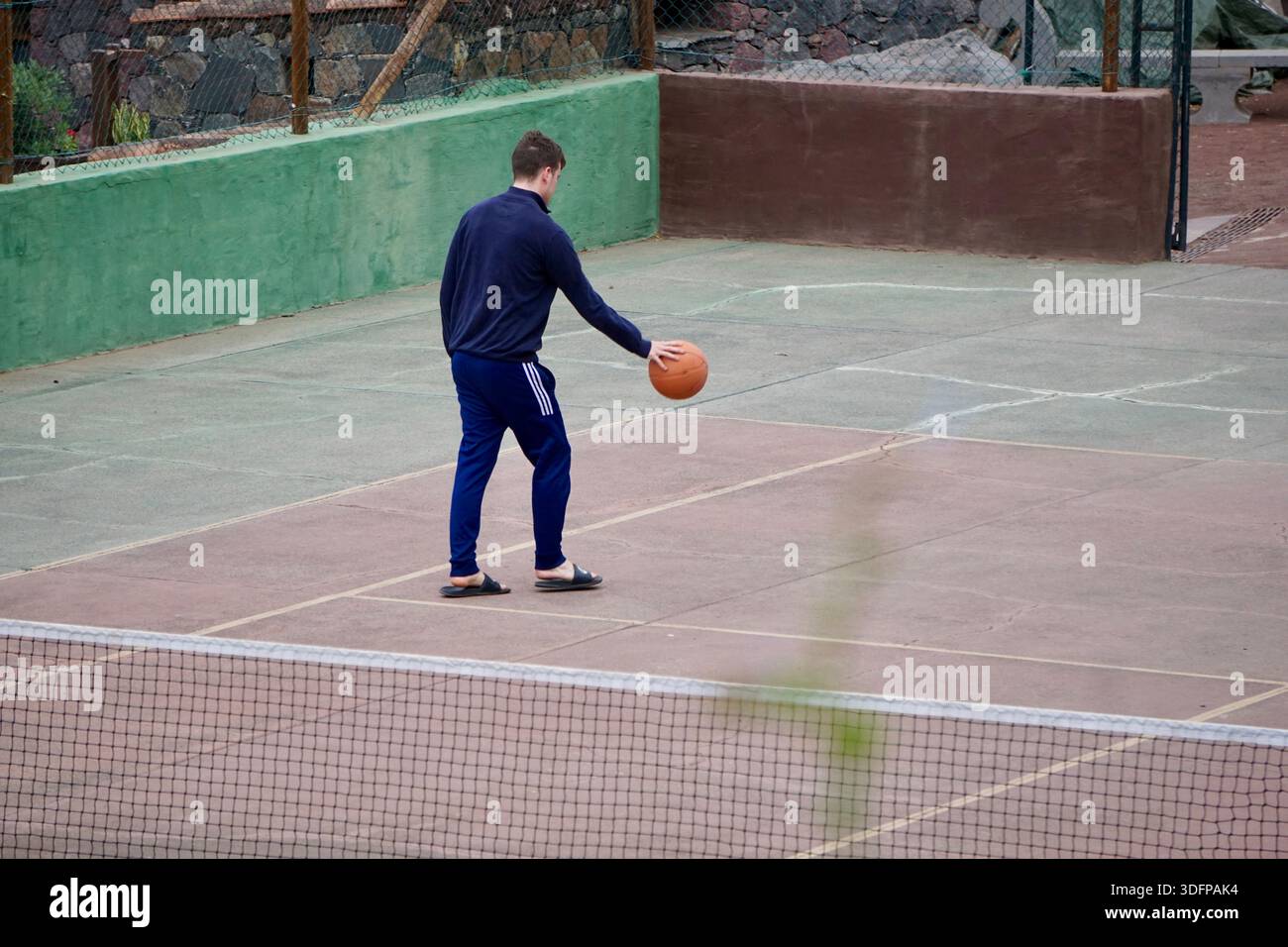 Ein Mann übt Basketball allein auf einem Platz im Freien und dribbelt den Ball während eines zwanglosen Trainings Stockfoto