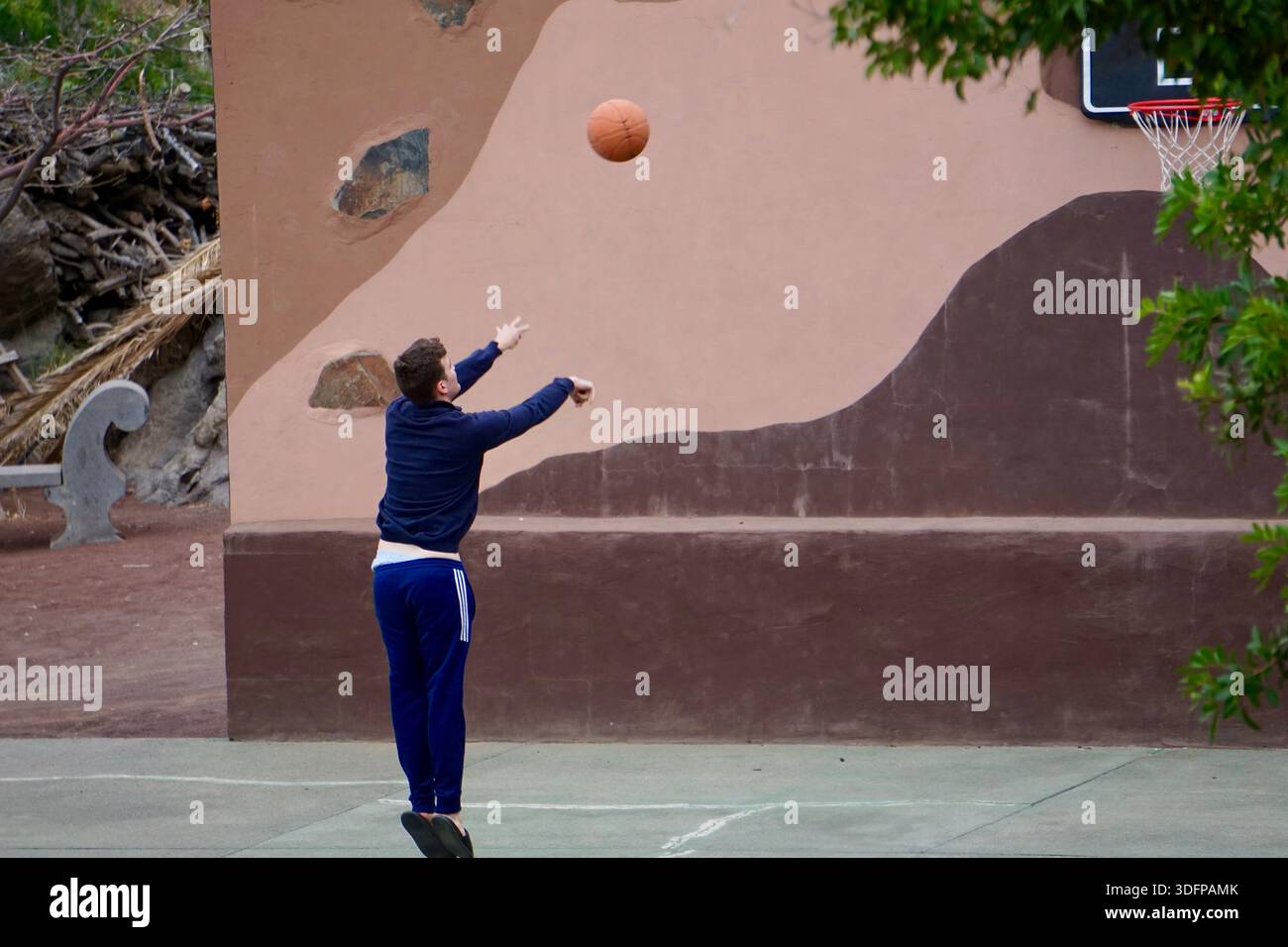 Mann, der Basketball allein auf einem Platz im Freien übt, während eines zwanglosen Trainings den Ball schießt Stockfoto