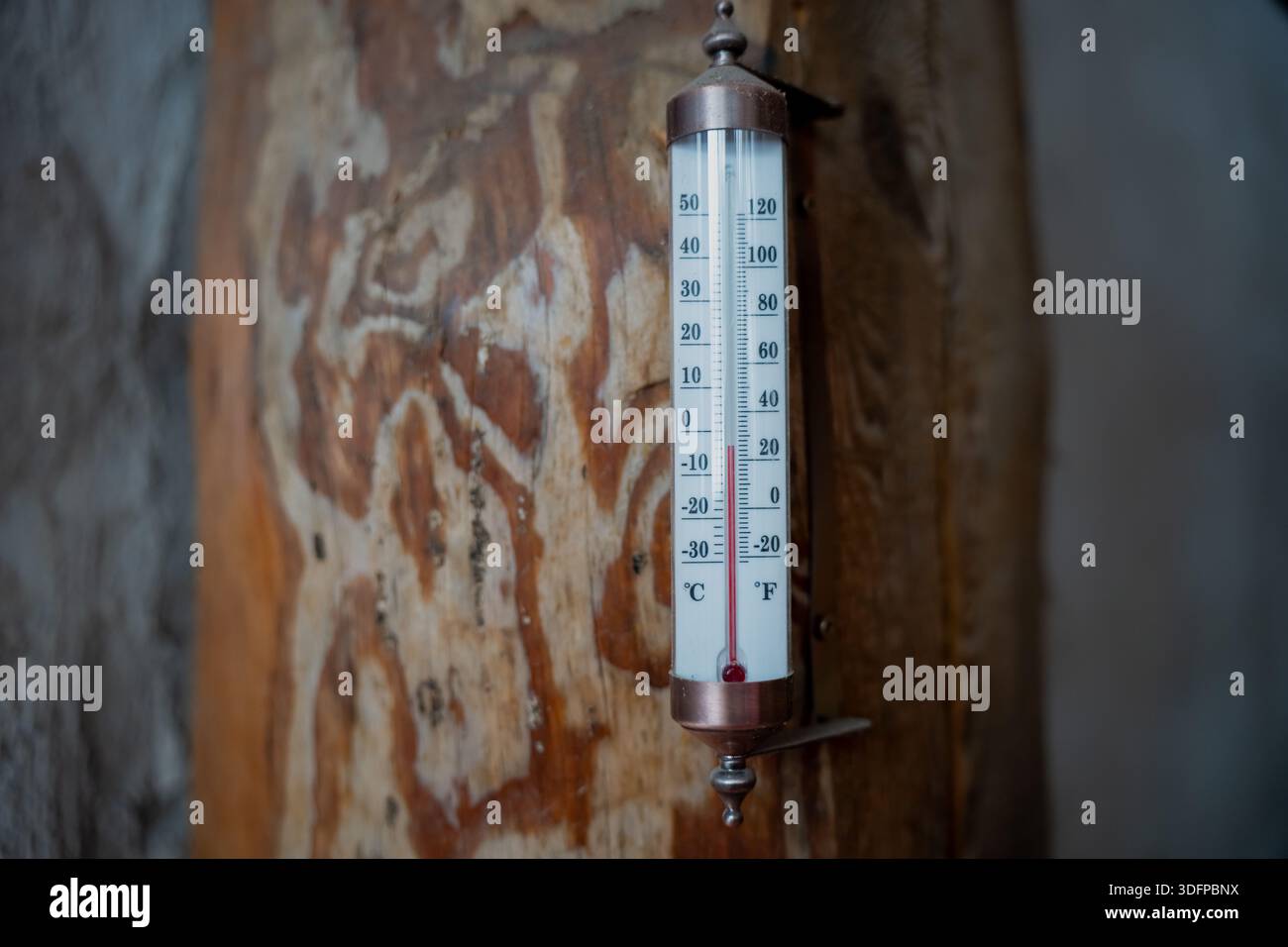 Vintage-Wandthermometer mit Celsius- und Fahrenheit-Skala, montiert auf rustikalem Holzbalken, Nahaufnahme des Innenraumtemperaturmessgeräts mit geringer Tiefe von Fie Stockfoto