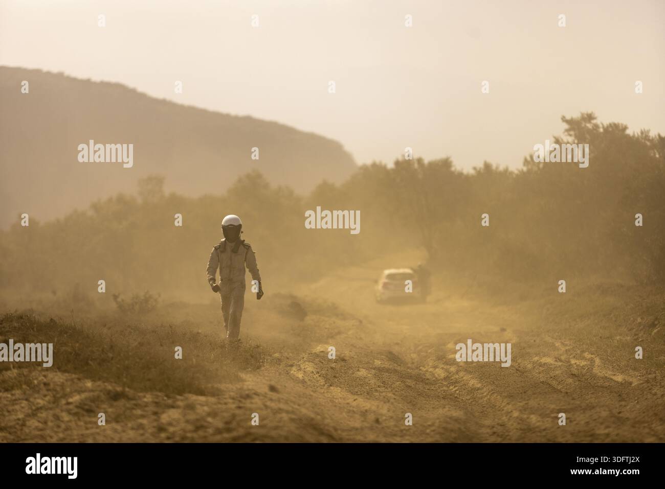 Naivasha, Kenia - 27. Juni 2021: Blick auf eine einsame Figur in einem weißen Anzug, die durch eine staubige Landschaft geht, die Luft ist dicht mit einem sepiafarbenen Dunst und einem Stockfoto