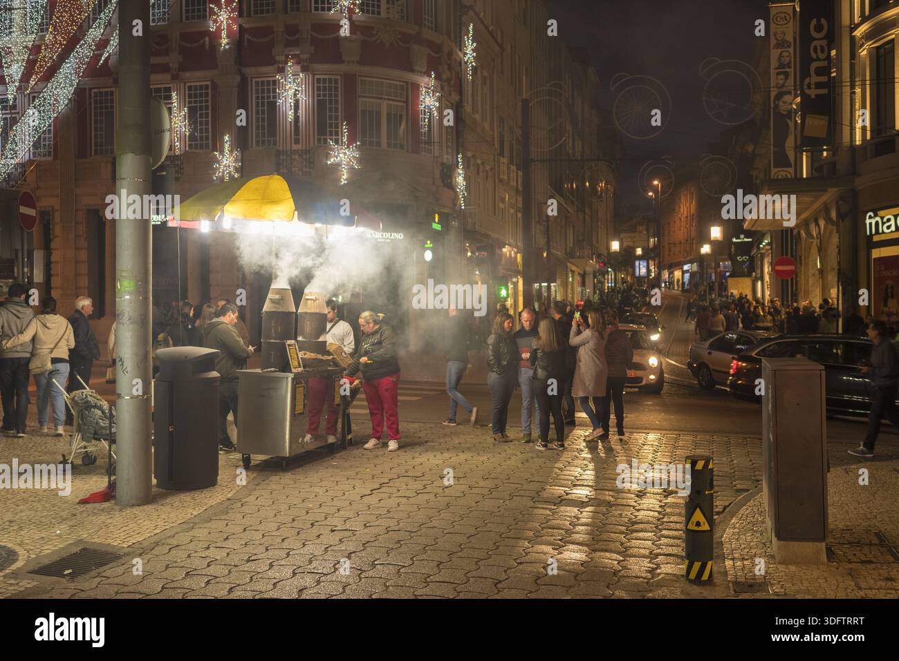 Porto, Portugal - 26. November 2017: Blick auf eine belebte Straßenszene mit einem verrauchten Stand eines Kastanienverkäufers, beleuchtet von festlichen Lichtern in der Nähe des berühmten Stockfoto