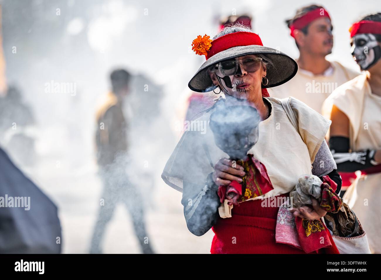 Mexiko-Stadt, Mexiko - 4. November 2023: Blick auf einen Straßenkünstler bei der Day of the Dead-Parade, geschmückt in leuchtendem Rot und weiß, in dem Rauch bläst Stockfoto