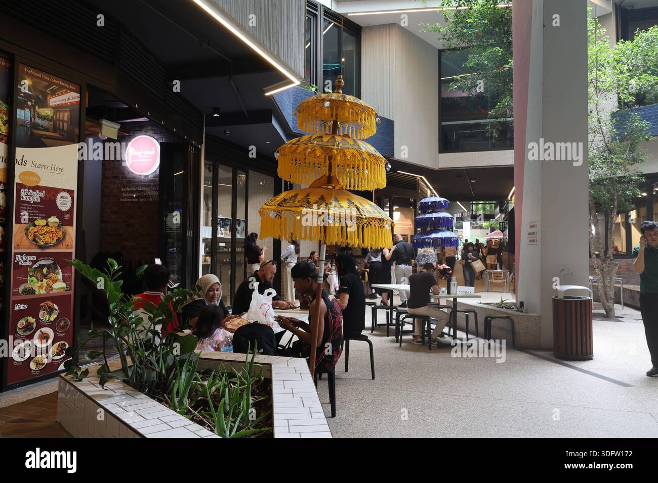 Asiatisches Restaurant im Café-Stil mit farbenfrohen Stufenschirmen draußen, Abendessen an Tischen und einem vom Boden bis zur Decke reichenden Menü in einem belebten Fußweg. Stockfoto