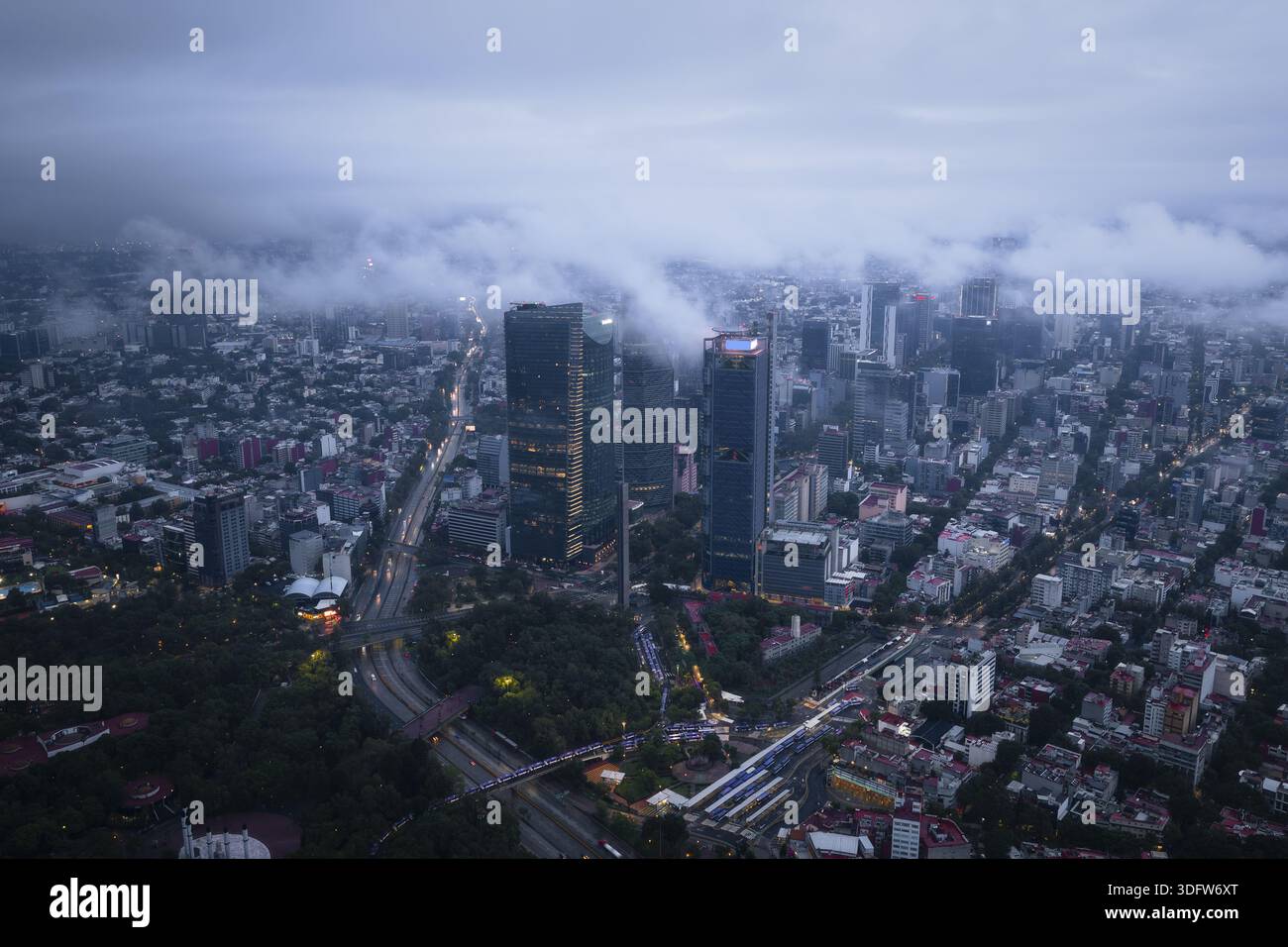 Aus der Vogelperspektive ziehen Wolkenkratzer durch den Nebel und werfen lange Schatten über Paseo de la Reformas geschäftige Straßen in Mexiko-Stadt, Mexiko. Stockfoto