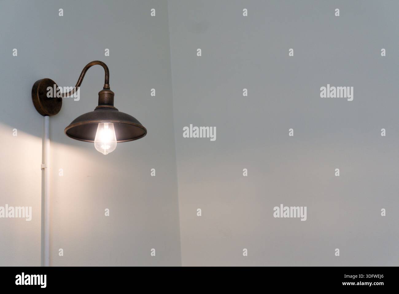 Eine Leuchte mit einer Lampe hängt an einer Wand. Die Leuchte ist eingeschaltet, und die Leuchte besteht aus Metall Stockfoto