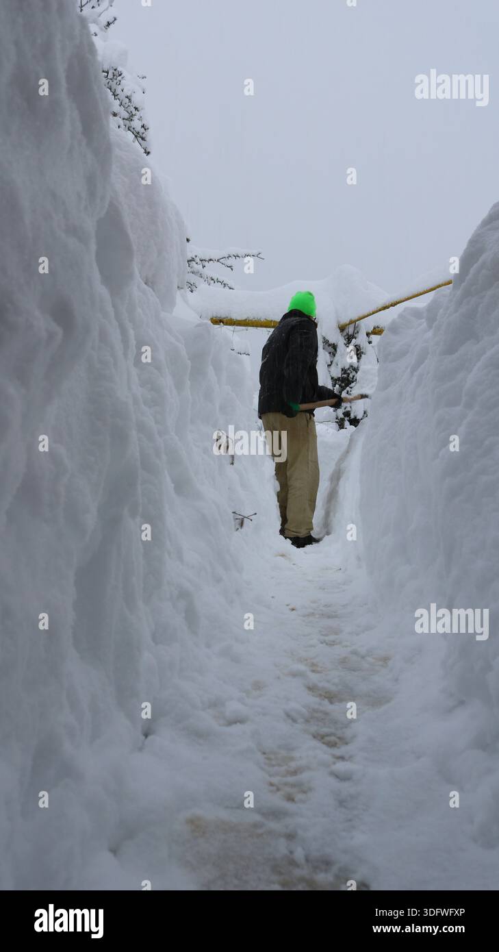 Ein Mann in dunkler Kleidung räumt einen Weg durch hohe Schneewehungen und schafft einen Schneetunnel. Die Folgen eines ungewöhnlichen Schneefalls in einem Dorf. Stockfoto