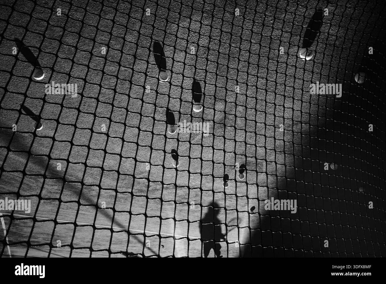 Tennisbälle ruhen auf einem Tonplatz, der durch einen Maschendrahtzaun in Schwarz-weiß gesehen wird. Eine menschliche Silhouette zieht sich über den Rahmen Stockfoto