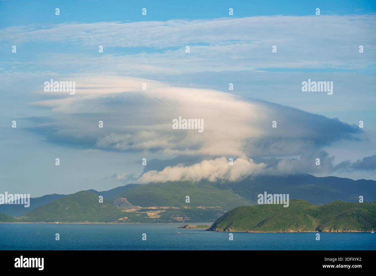 Die dramatische Wolkenbildung der Lentikularplatten schweben über sanften grünen Hügeln und Küstenbergen. Der hellblaue Himmel ist ein wunderschöner Kontrast zum Stockfoto