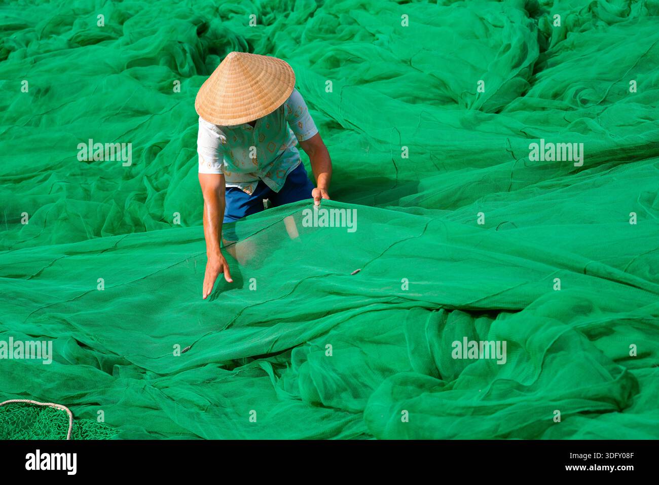Mann Guy in traditionellem authentischem Hut vietnamesisches Entwirren grüner Fischernetze, die sich auf das Angeln vorbereiten und auf das Meer gehen. Stockfoto
