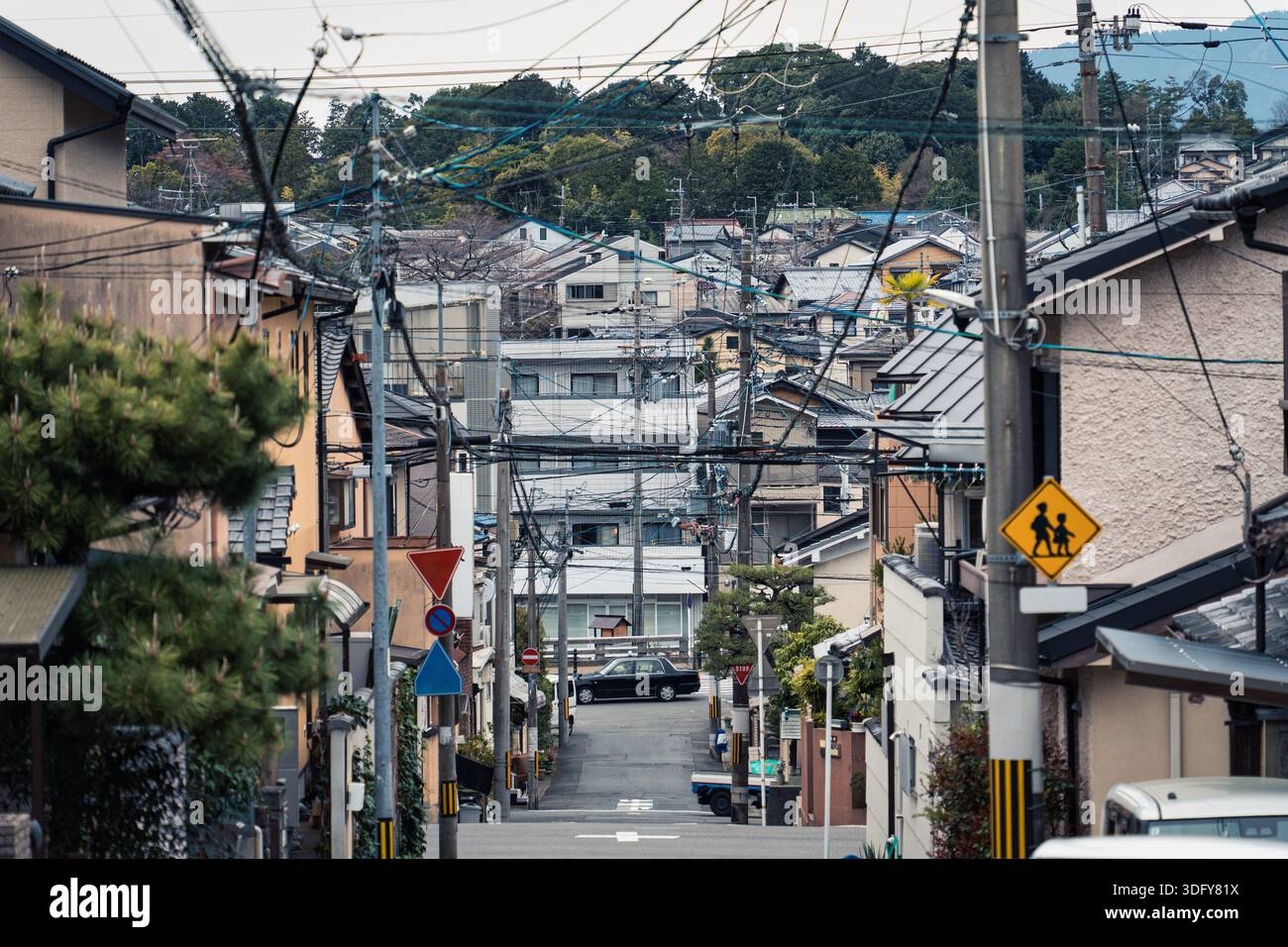 Traditionelles, dichtes Gebäude an einer ruhigen Wohnstraße, Stromleitungen über dem Kopf, Verkehrszeichen und Auto im Vorstadtgebiet von Kyoto, Japan Stockfoto