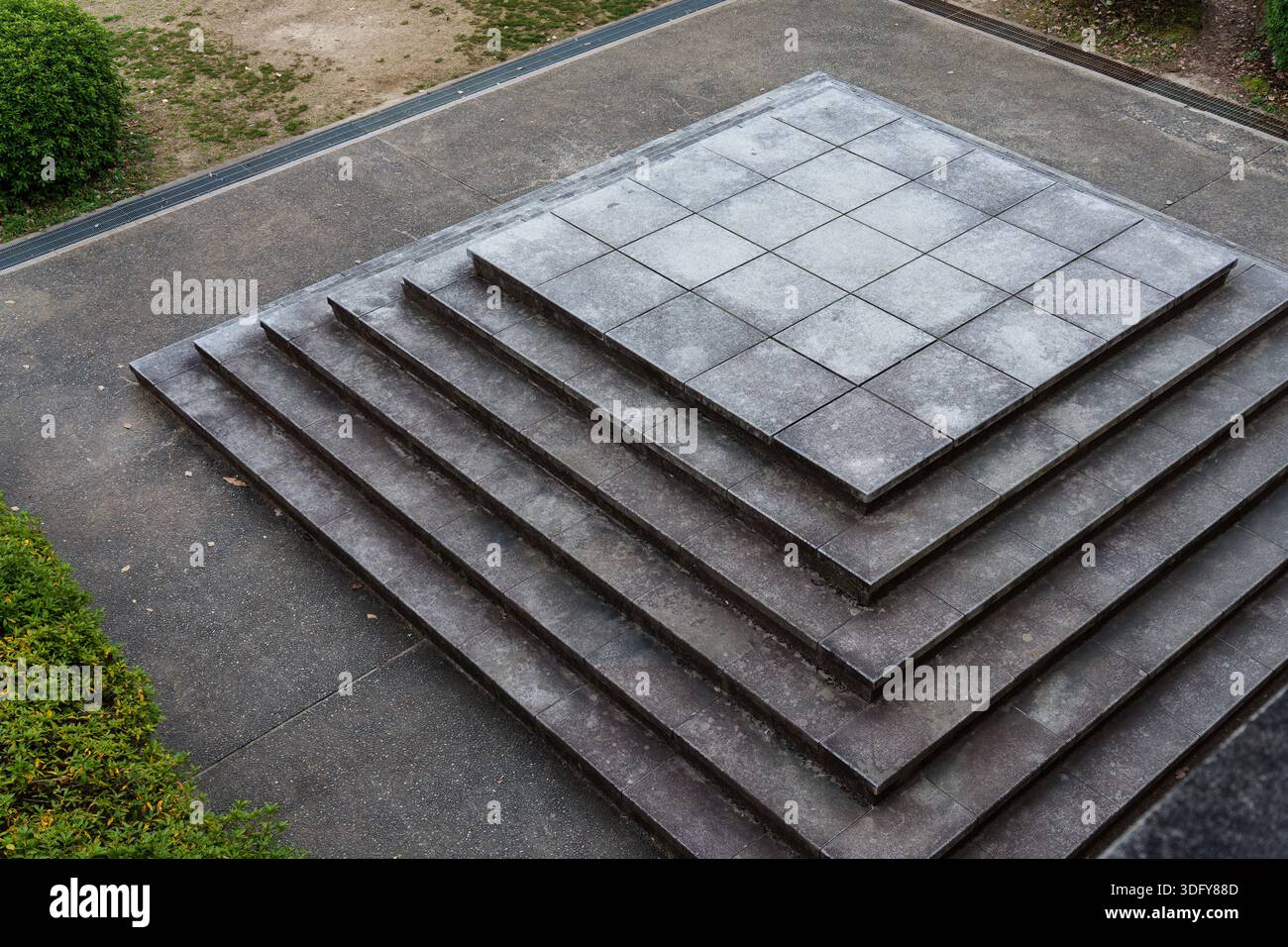 Geometrische Betonplattform mit mehrschichtigen Steinstufen, die eine symmetrische architektonische Struktur im öffentlichen Raum im Freien bilden Stockfoto