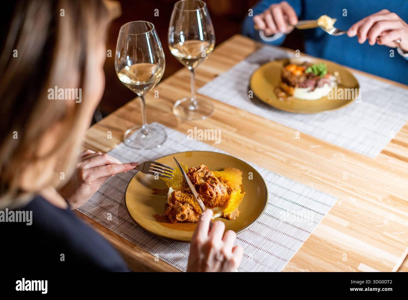 Zwei Personen sitzen an einem Holztisch mit Gläsern Wein. Sie essen zu Abend, mit Tellern mit Essen vor ihnen. Die Atmosphäre ist warm und einladend Stockfoto