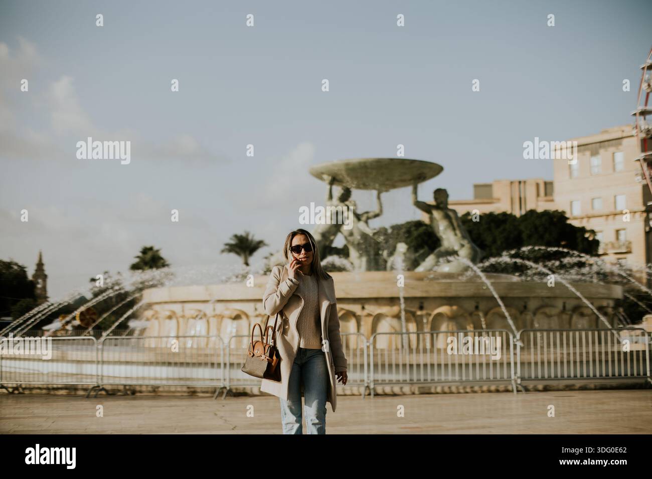 Eine Frau läuft vor einem großen Brunnen in Malta. Sie genießt das warme Wetter. Der Brunnen ist mit Skulpturen und Wasserspritzern in einer lebhaften Einrichtung ausgestattet Stockfoto