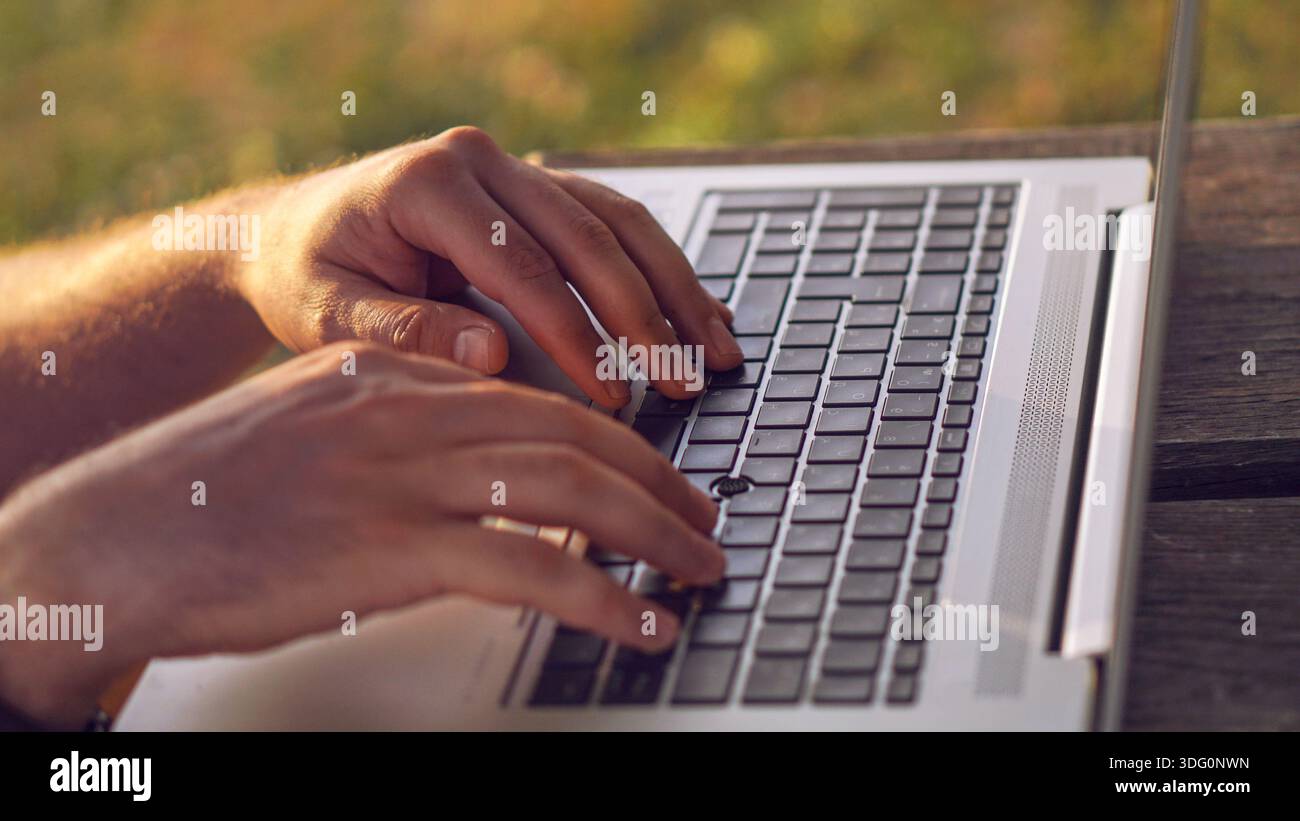 Nahaufnahme von digitalen Nomaden-Freiberuflern, die auf einem Laptop tippen. Nahaufnahme von Händen, die draußen auf einem Laptop auf einem Holztisch tippen. Stockfoto