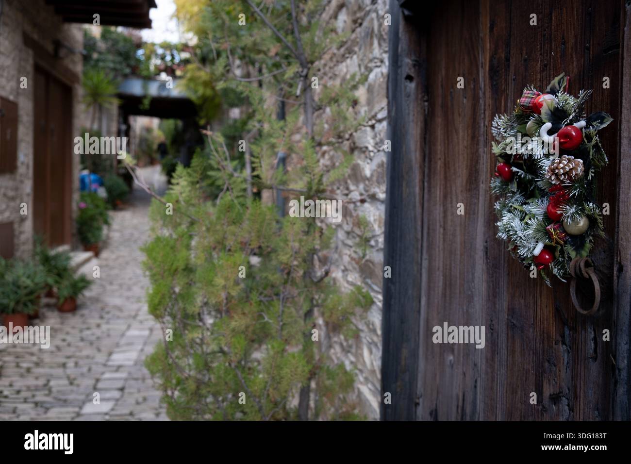 Festlicher weihnachtskranz, der an einer alten Holztür hängt, unterstreicht die charmante Atmosphäre einer traditionellen Dorfstraße aus Stein. Lefkara Village Cypru Stockfoto
