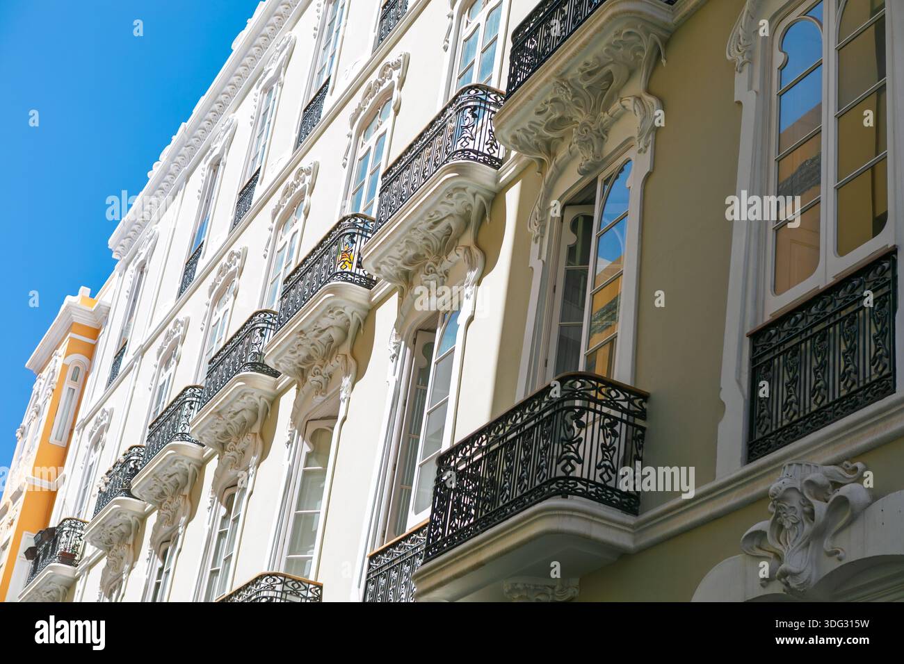 Blick nach oben auf die mehrstöckige Fassade des historischen Gebäudes mit kunstvollen Stuckschnitzereien und schmiedeeisernen Balkonen. Architektonische Mischung aus neoklassizistischem Stil Stockfoto