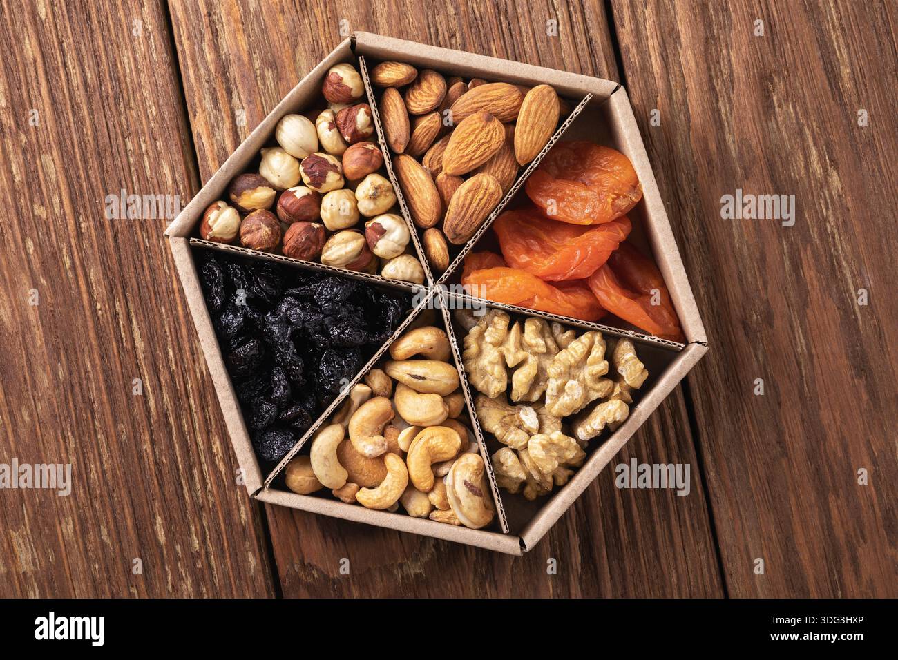 Verschiedene Nüsse und getrocknete Früchte in einer Pappschachtel auf einem Holztisch, Draufsicht, authentisches Foto, nicht AI-generiert Stockfoto