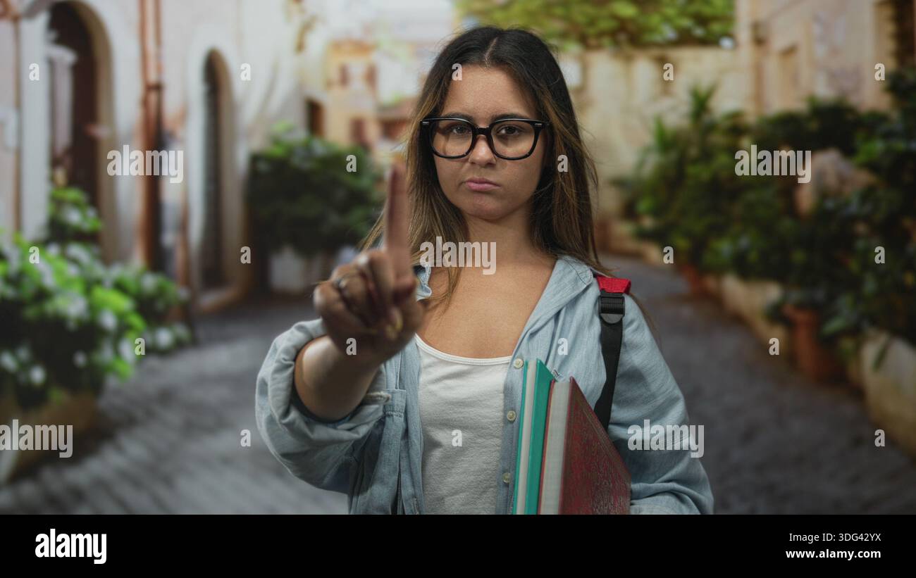 Frau zeigt den Finger in der Straße nach vorne, hält Notizbücher und Rucksack, während sie Brille und Jeansshirt trägt; Bestimmungsgrenze. Stockfoto
