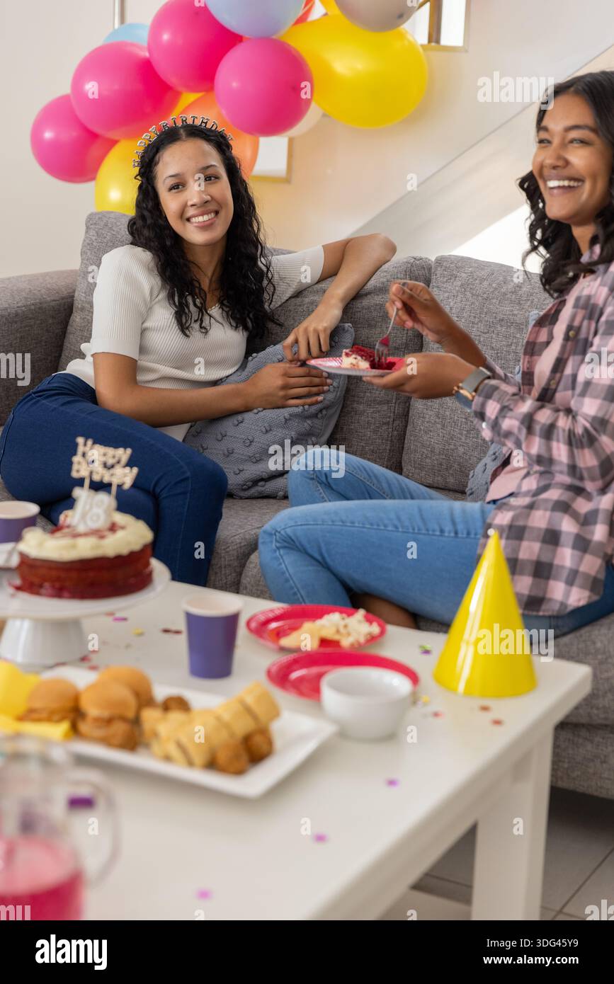 Vielfältige Mutter und Tochter im Teenageralter sitzen auf dem Sofa und feiern Geburtstag mit rotem Samtkuchen Stockfoto