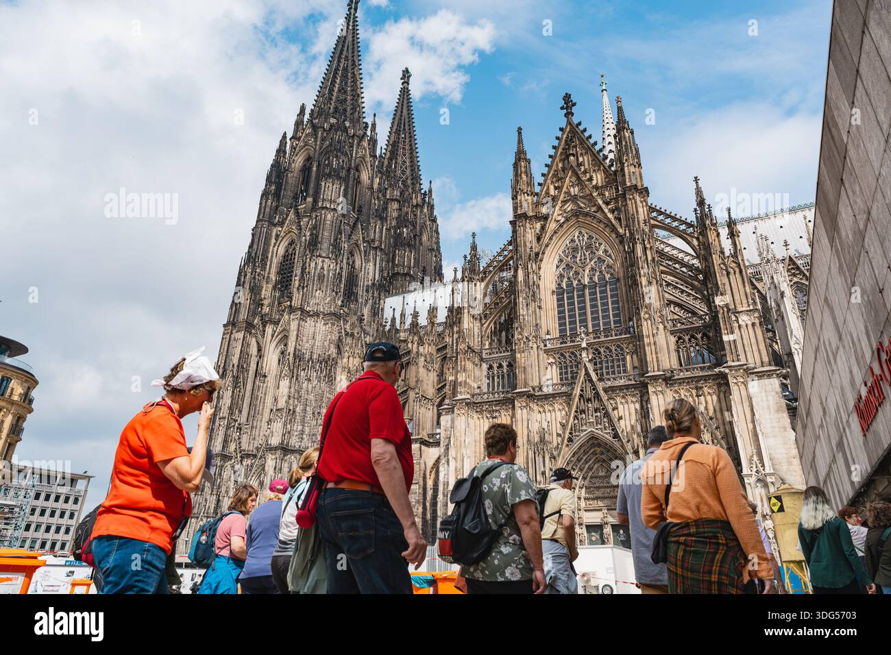 Touristen, die in der Nähe der majestätischen gotischen Kölner Domfassade spazieren Stockfoto
