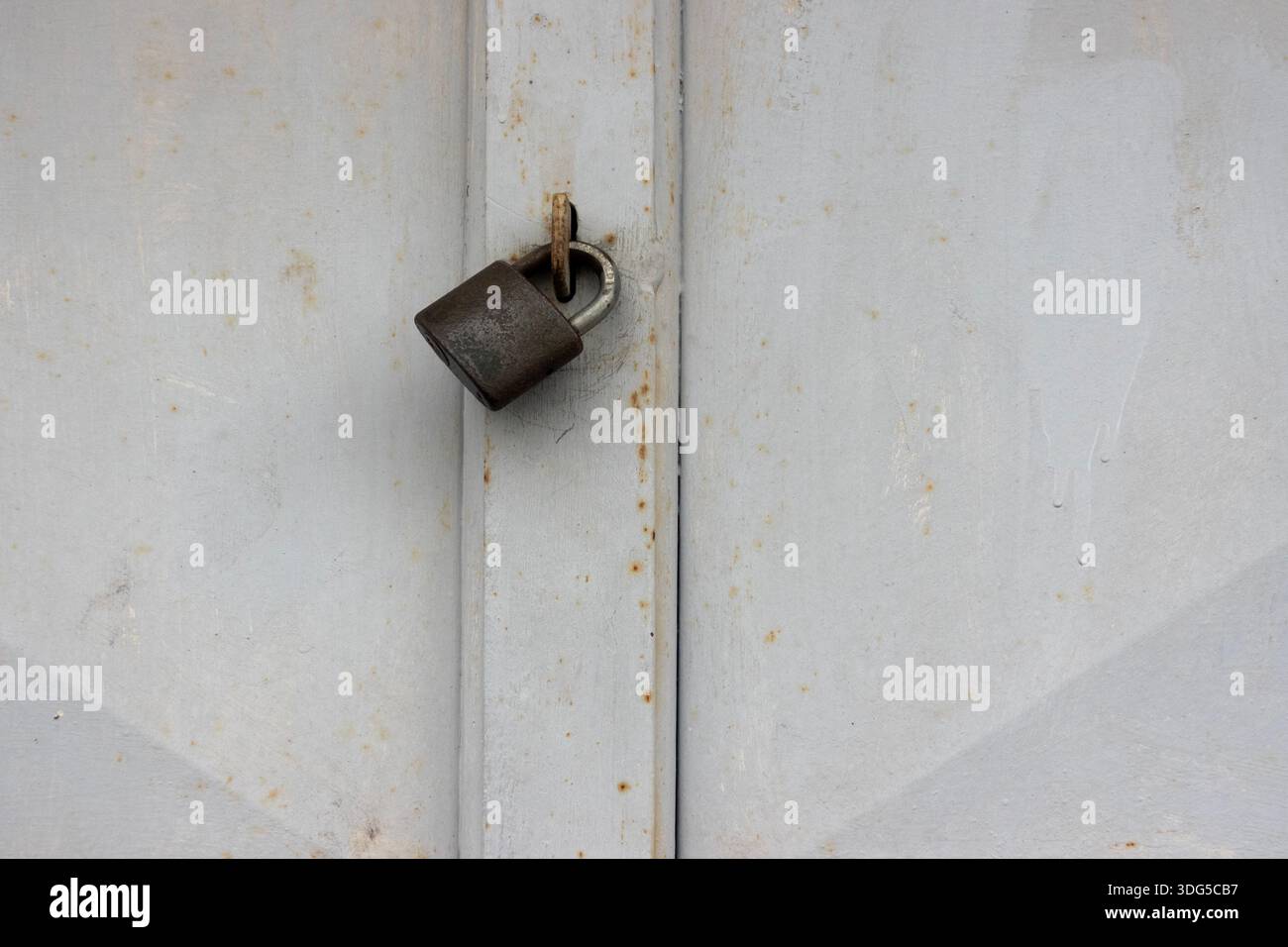 Weiße Metalltür mit einem Vorhängeschloss gesichert, symbolisiert Sicherheit, Privatsphäre und eingeschränkten Zugang Stockfoto