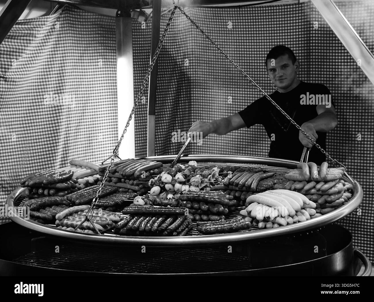 PARIS - November 30: Ein nicht identifizierter junger Mann kocht eine Auswahl gegrillter Würstchen und Kebabs auf einem großen Hängegrill auf dem Weihnachtsmarkt am 30. November 201 Stockfoto