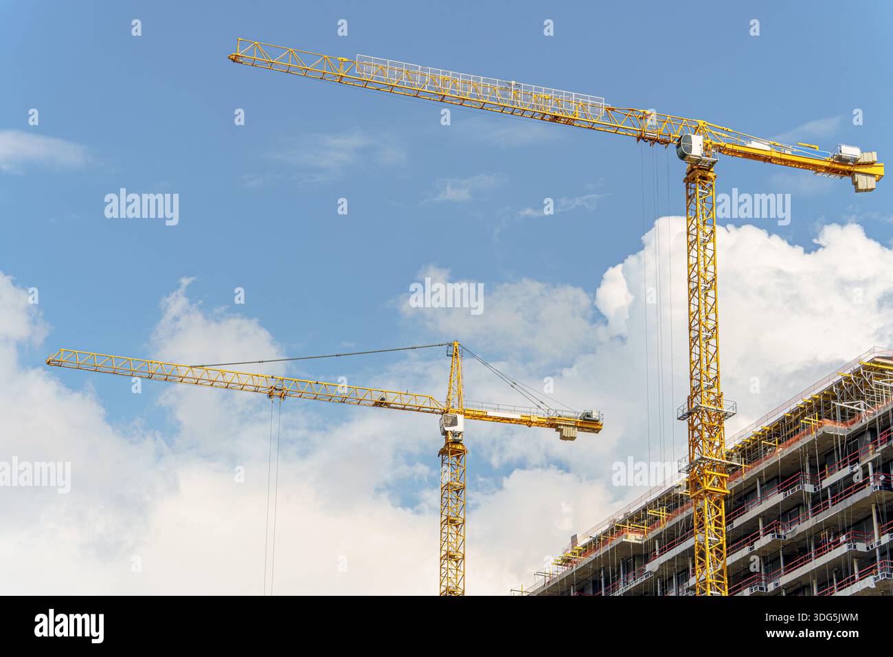 Vor dem blauen Himmel bauen zwei Baukräne ein mehrstöckiges Gebäude, das das rasante Tempo der Stadtentwicklung unterstreicht. Die Maschinen und Stockfoto