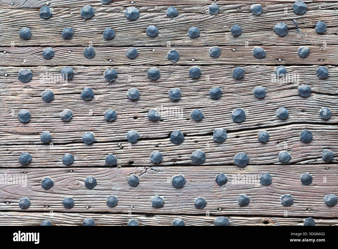 Architektonische Details einer antiken mittelalterlichen Tür mit handgeschmiedeten Eisenbolzen oder Nägeln für strukturelle Unterstützung, Schutz und verwitterte Holzdielen Stockfoto