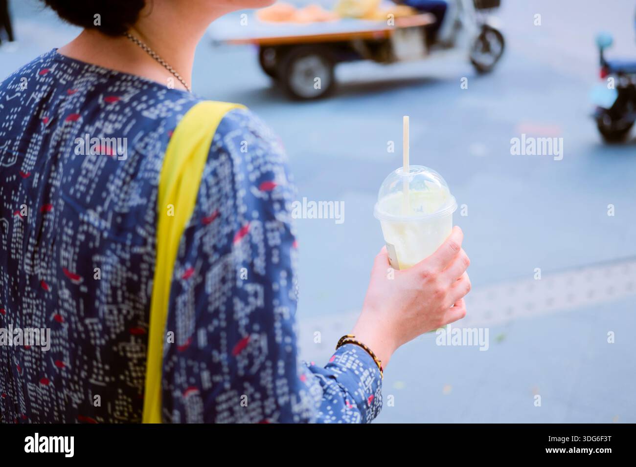 Person in blauem Hemd mit kaltem Getränk auf einer belebten Straße. Guangzhou, Guangdong, China Stockfoto
