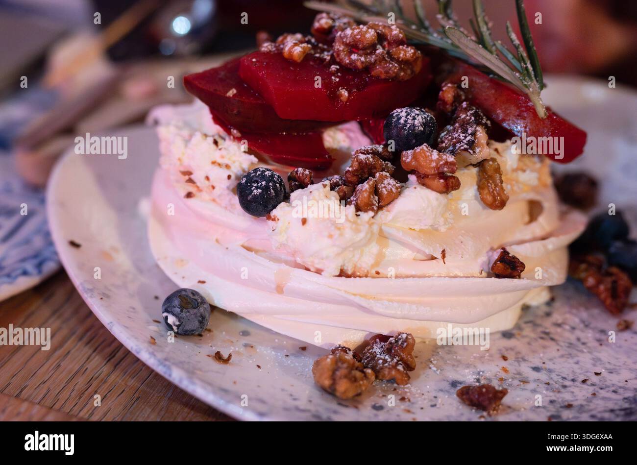 Ein klassisches Eiweiß-Meringue pavlova-Dessert mit roter Fruchtsauce, garniert mit Walnüssen und Beeren Stockfoto