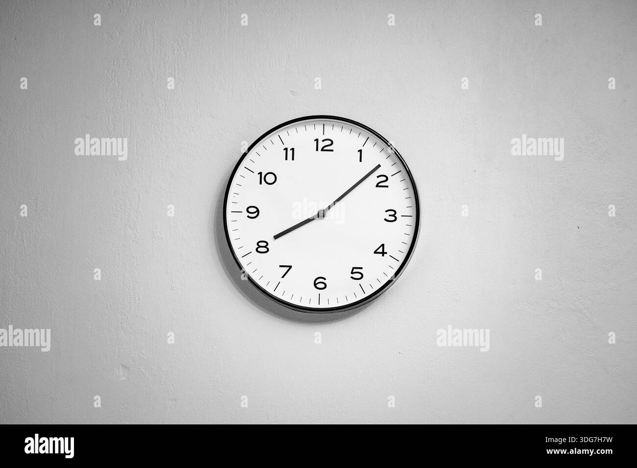 Wanduhr an einer leeren Wand. Minimalistischer Innenhintergrund mit einer einzigen Uhr, die an einer leeren Wand hängt, symbolisiert Zeit, Warten, Einfachheit. Stockfoto