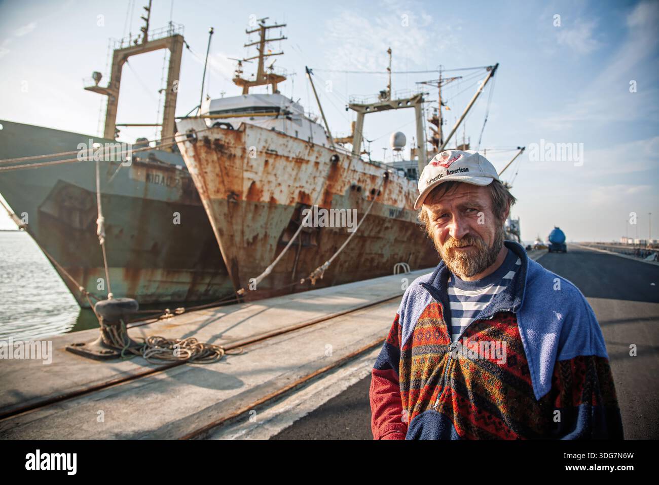 Ein ukrainischer Seemann posiert vor seinem rostigen Fischerboot in Huelva, Spanien, und zeigt das maritime Leben und die internationale Präsenz in der Hafenstadt. Stockfoto