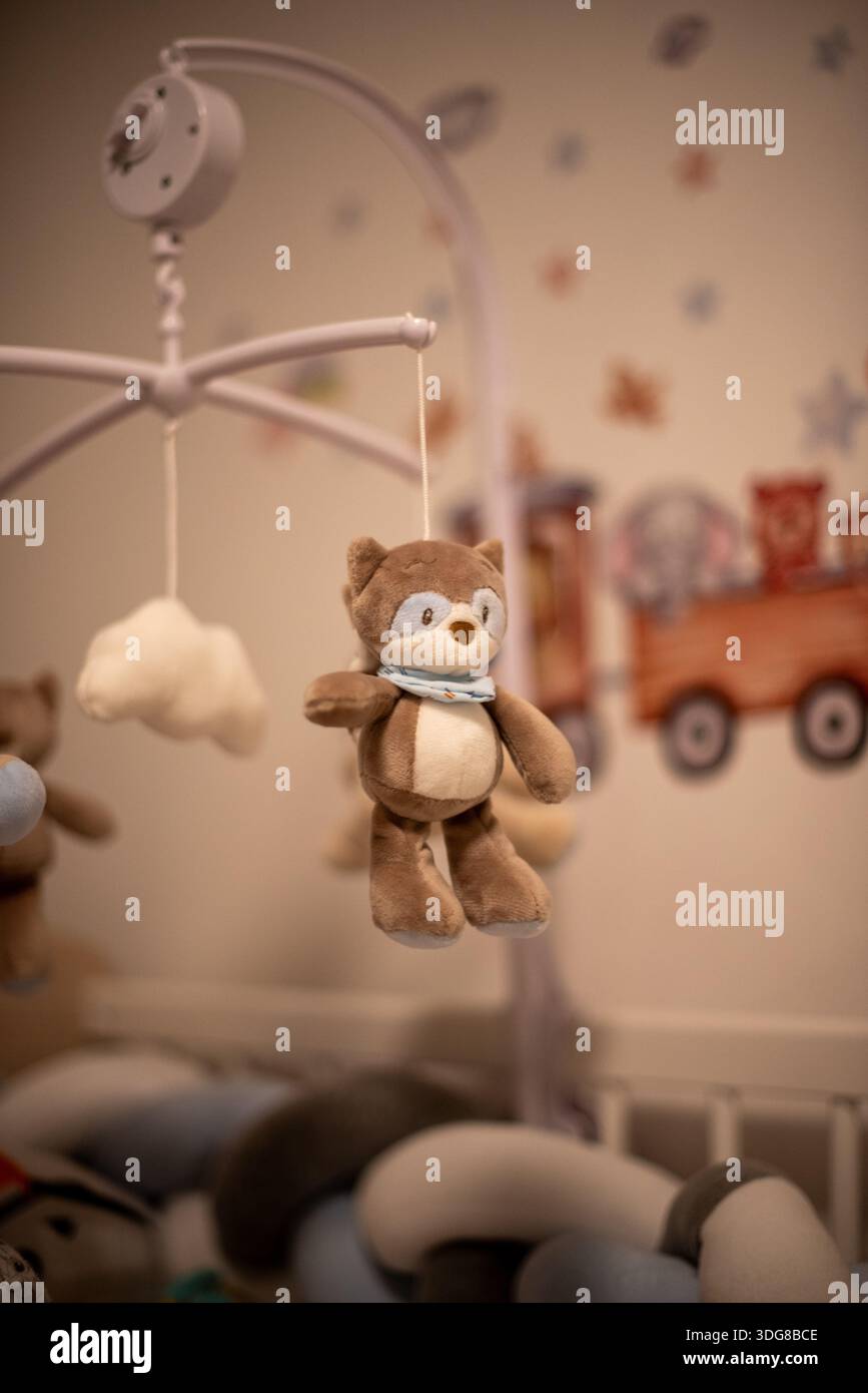 Niedliches Kuscheltier, das an einem Babybett hängt, sorgt für eine warme und behagliche Atmosphäre im Kinderzimmer mit weichem Fokus und sanftem Licht. Stockfoto
