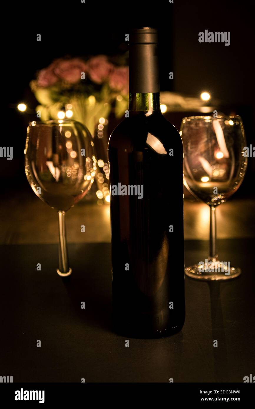 Weinflasche aus nächster Nähe mit zwei Gläsern und goldenen Bokeh-Lichtern, geringe Schärfentiefe für eine warme, intime Atmosphäre. Stockfoto
