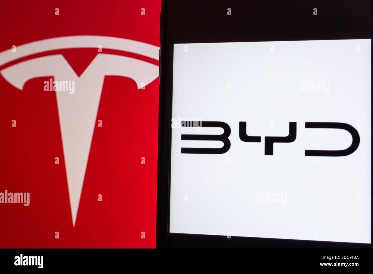 Quito, ECUADOR - 7. Januar 2026 : auf separaten Bildschirmen werden die Logos der Hersteller Tesla und BYD für Elektrofahrzeuge angezeigt, die den Wettbewerb in der Elektrofahrzeugindustrie repräsentieren. Stockfoto