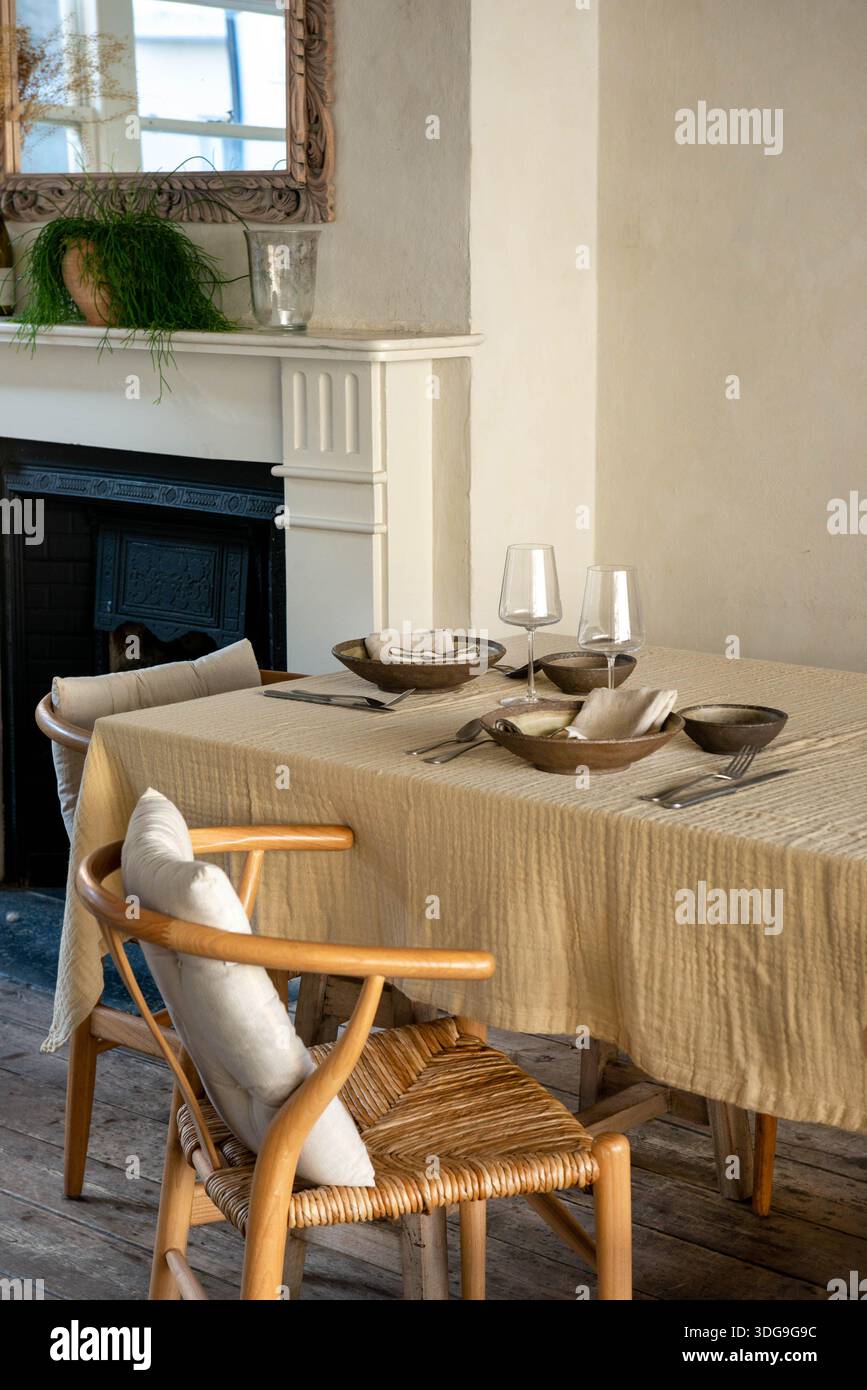 Ein wunderschön gestalteter Speisesaal mit einem Tisch mit dunklen Keramikschalen, Weingläsern und silbernem Besteck auf einem strukturierten gelben Leinentisch. Stockfoto