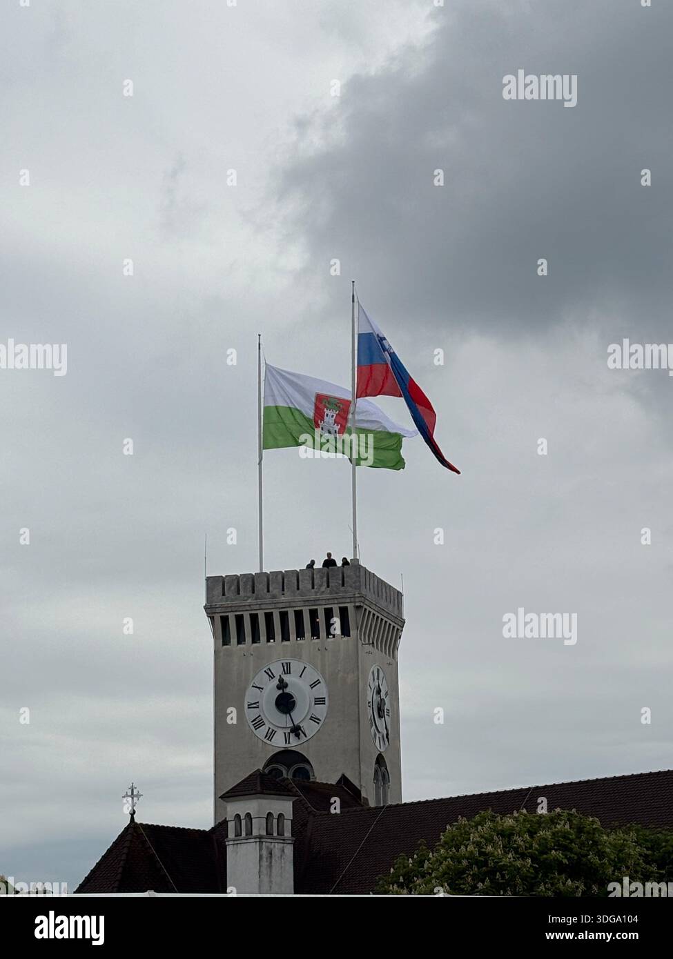 Glockenturm mit slowenischen und Ljubljana-Flaggen unter dramatischem bewölktem Himmel – bürgerliche Architektur in Slowenien. Stockfoto