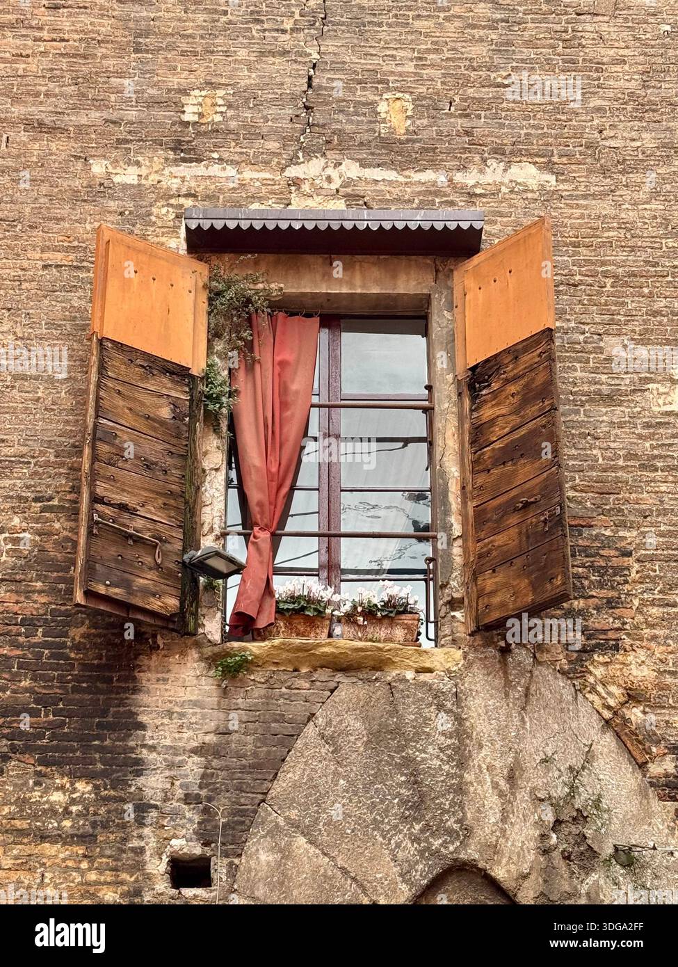 Öffnen Sie Holzläden an einem rustikalen Fenster eines alten italienischen Gebäudes, die Details des Alltags und verwitterte Texturen historischer Architektur enthüllen - Smartphone-aufgenommenes Stockfoto